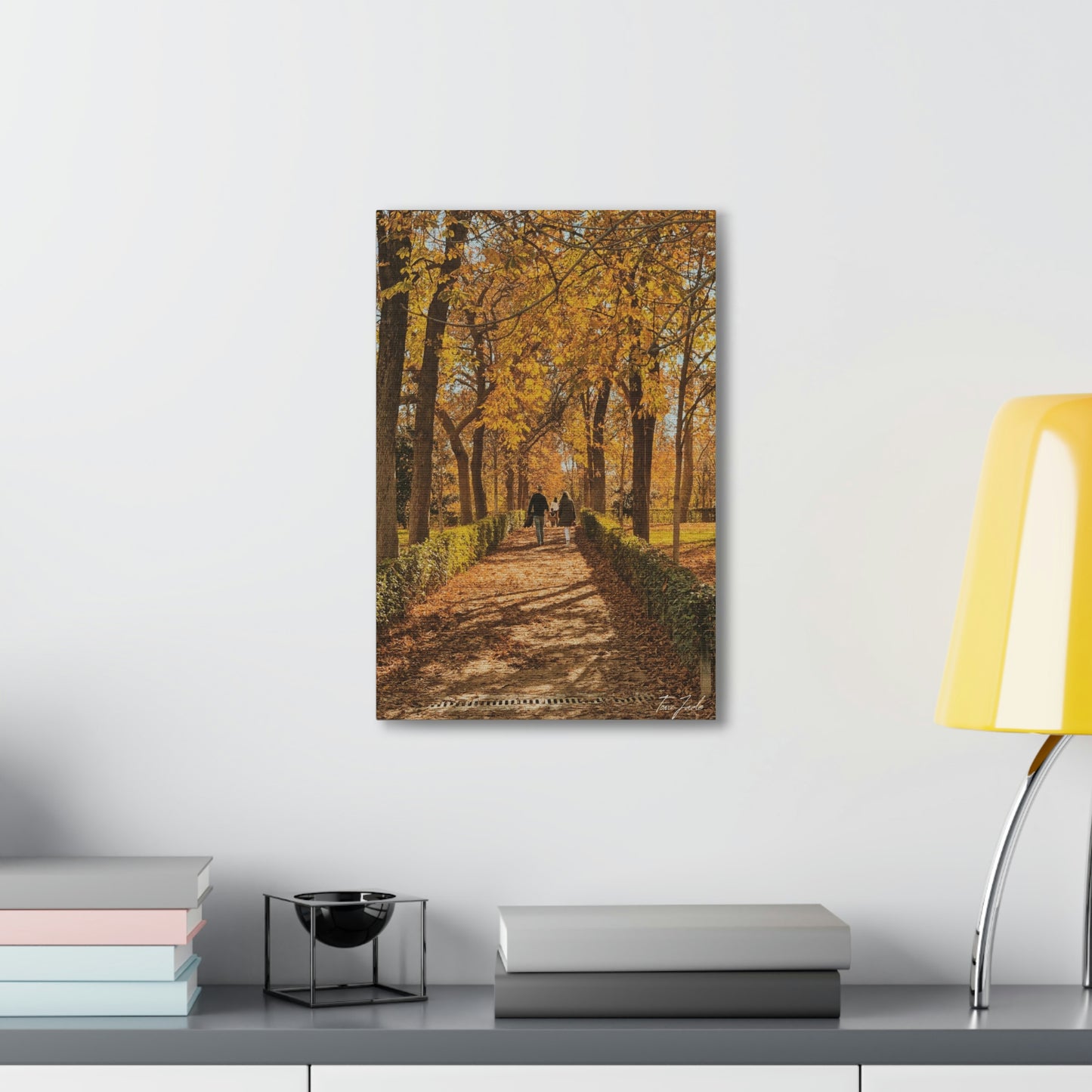 Our fall wall art in Spain is very colorful and vibrant. A couple is walking on the park trail with other families in front, the bright yellow leaves surrounding them. This canvas is a size 12 x 18. 